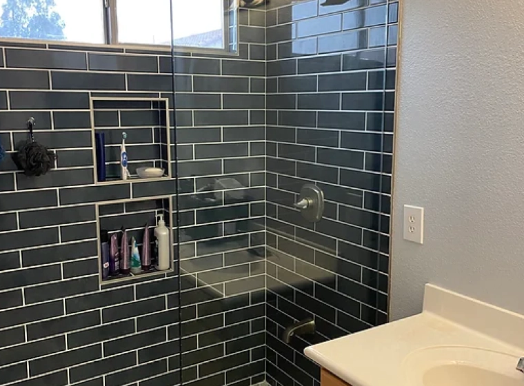 bathroom with dark gren greyish tiles and a glass door for the shower